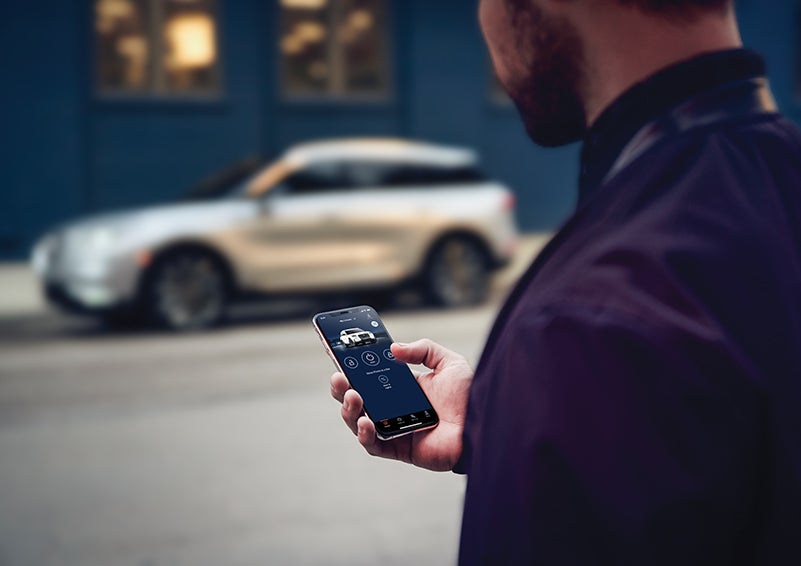 A person is shown interacting with a smartphone to connect to a Lincoln vehicle across the street. | Preston Lincoln in Hurlock MD